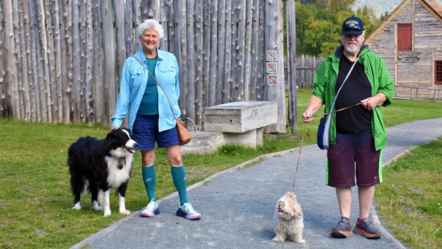 Two people with two dogs on leash, standing in front of a historic structure.